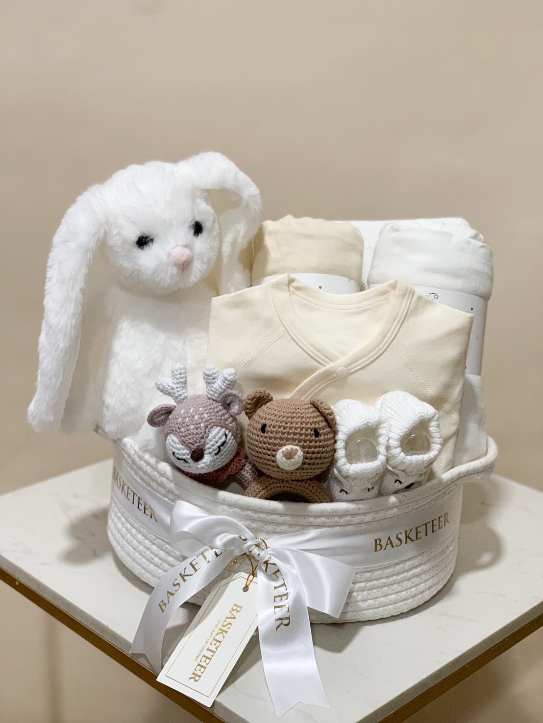 Neutral baby gift basket with plush toys, swaddle blankets, and newborn essentials.