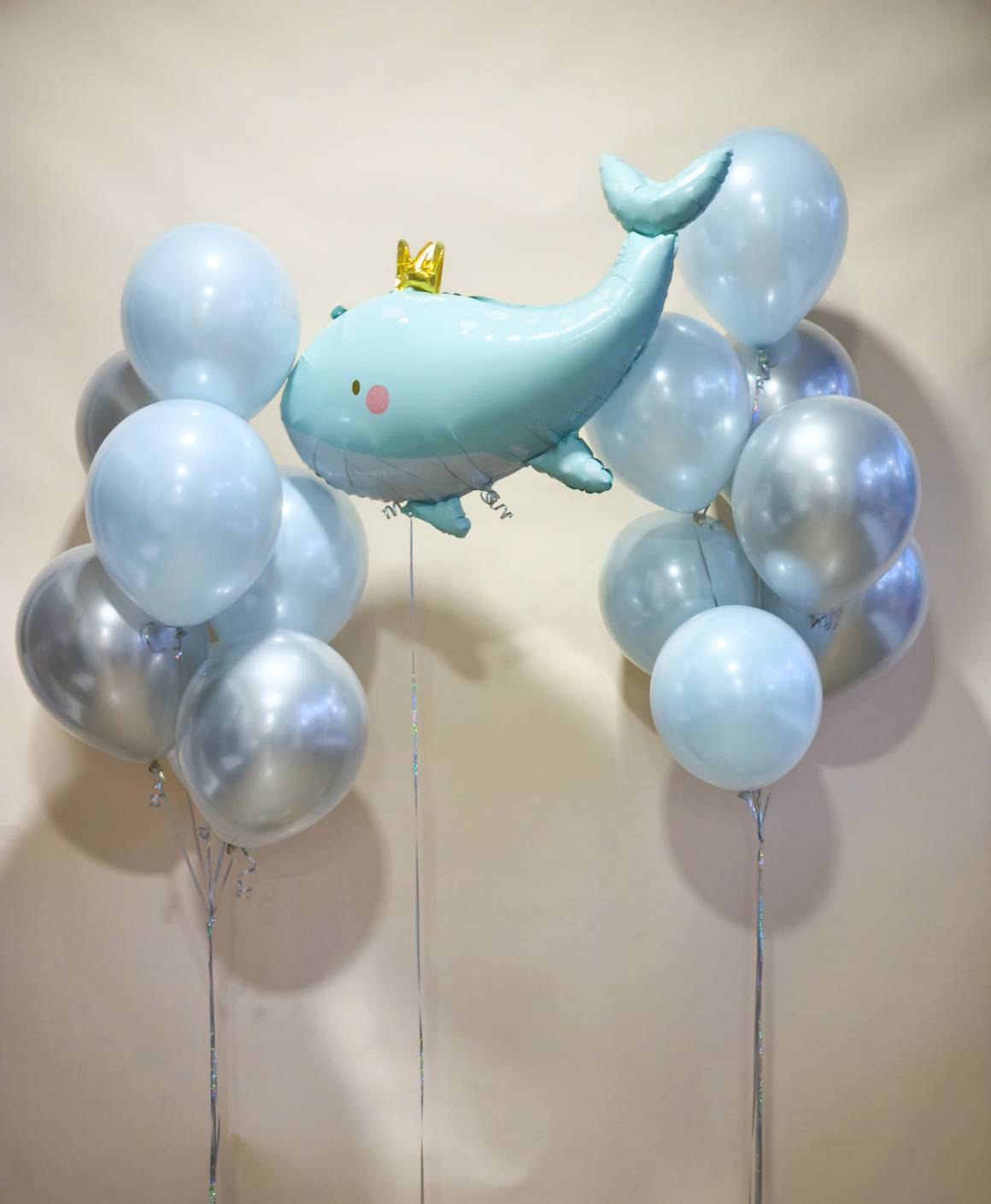 Cute blue whale foil balloon with crown, surrounded by metallic silver and light blue balloons.