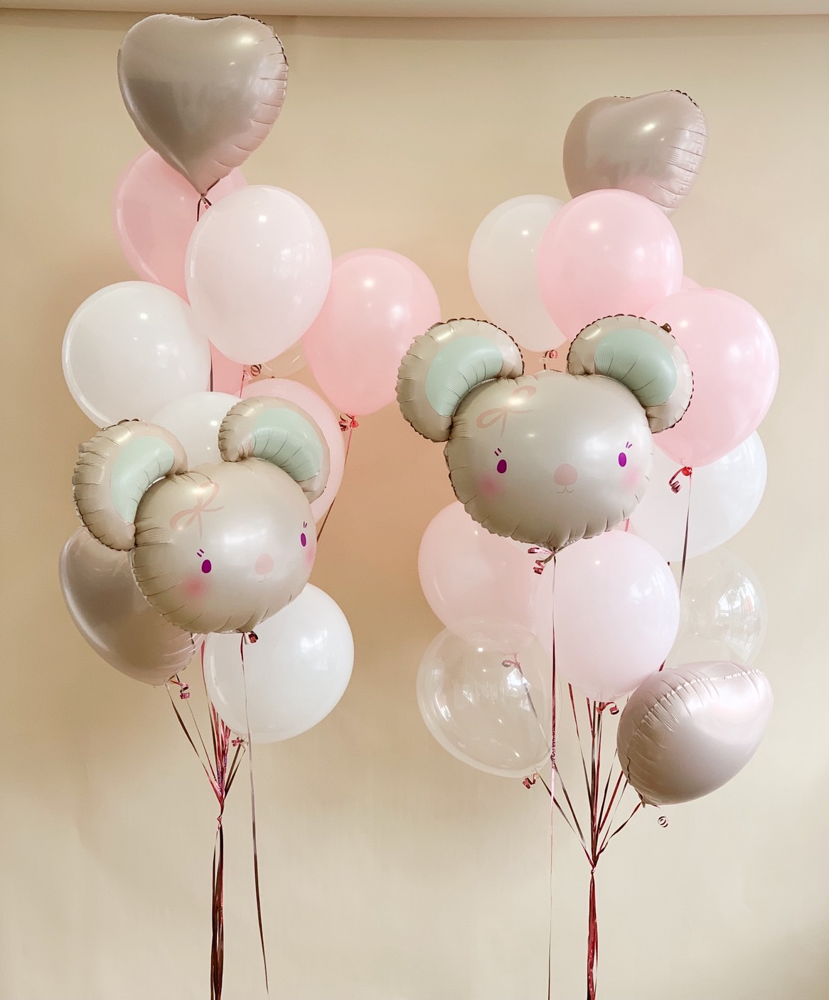 Adorable pastel pink and white balloon bouquet with bear face foil balloons and heart-shaped accents, perfect for baby girls.