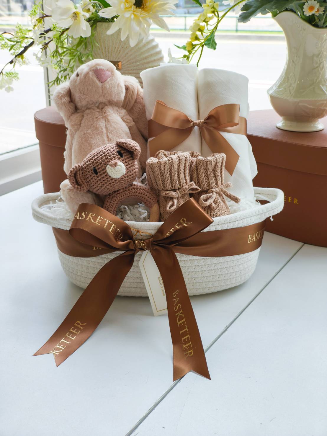 Premium baby gift basket with plush bunny, knitted teddy, blanket, baby booties, and newborn essentials, tied with luxury ribbon