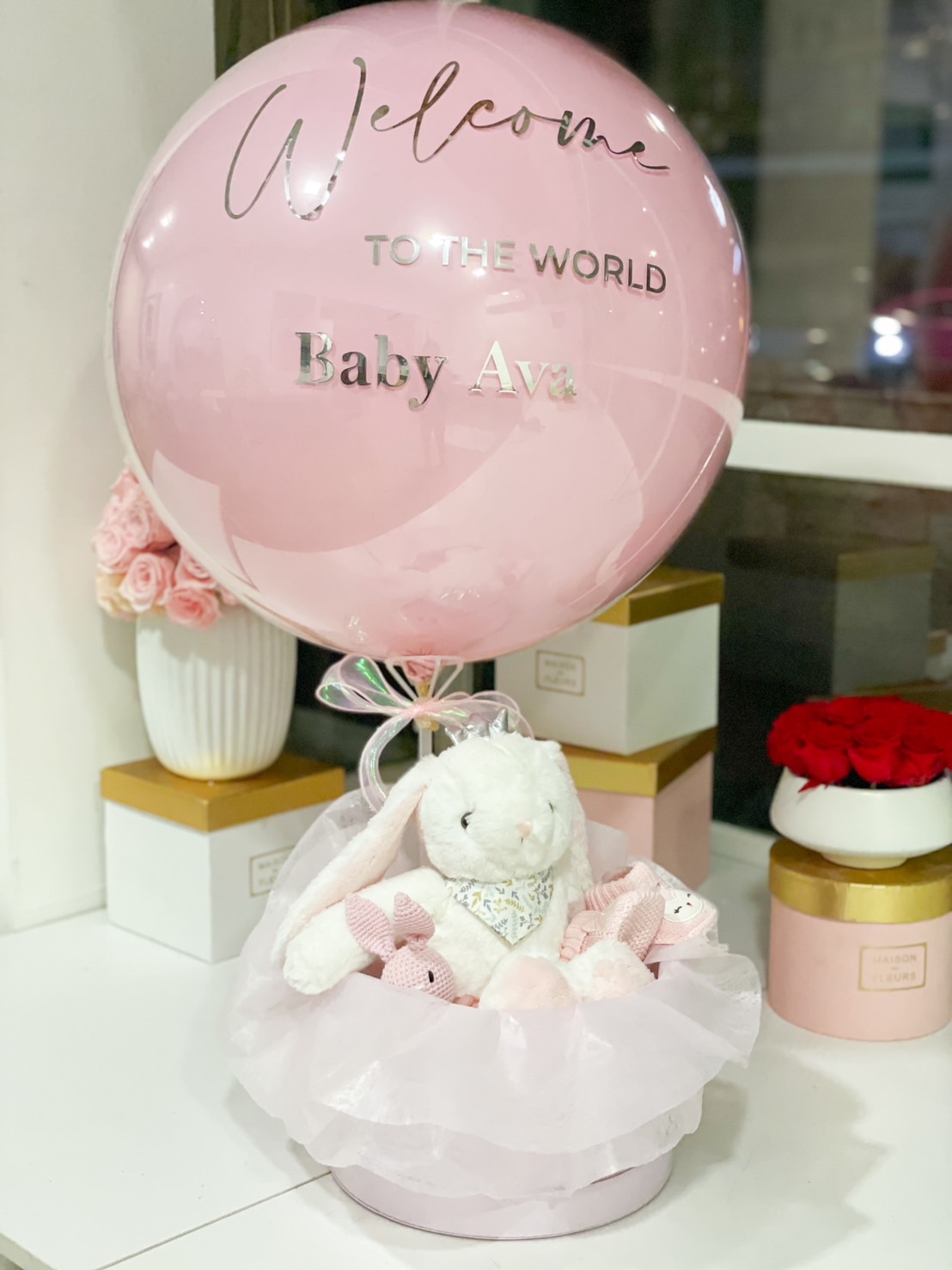 A newborn gift set featuring a soft white plush bunny, pink baby essentials, and a personalized balloon with 