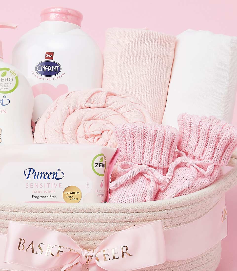 A pink baby gift basket filled with essential items, including baby lotion, powder, clothes, and a blanket.