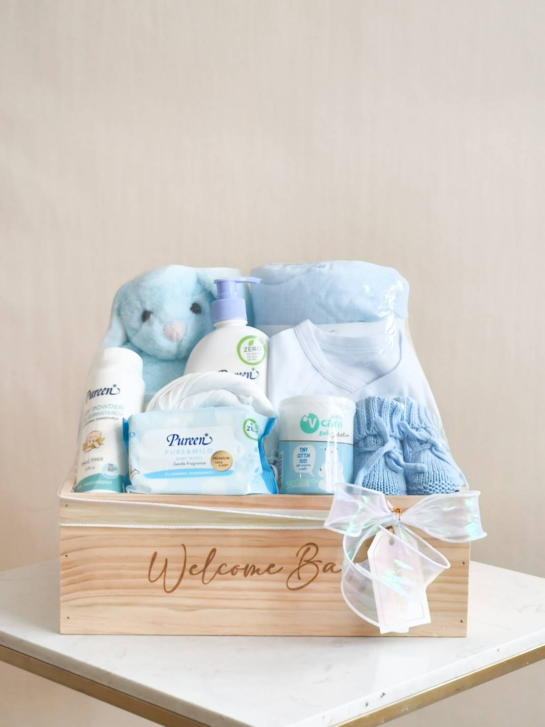 Baby boy welcome gift basket with blue clothing, skincare, wipes, and plush toy in a wooden box