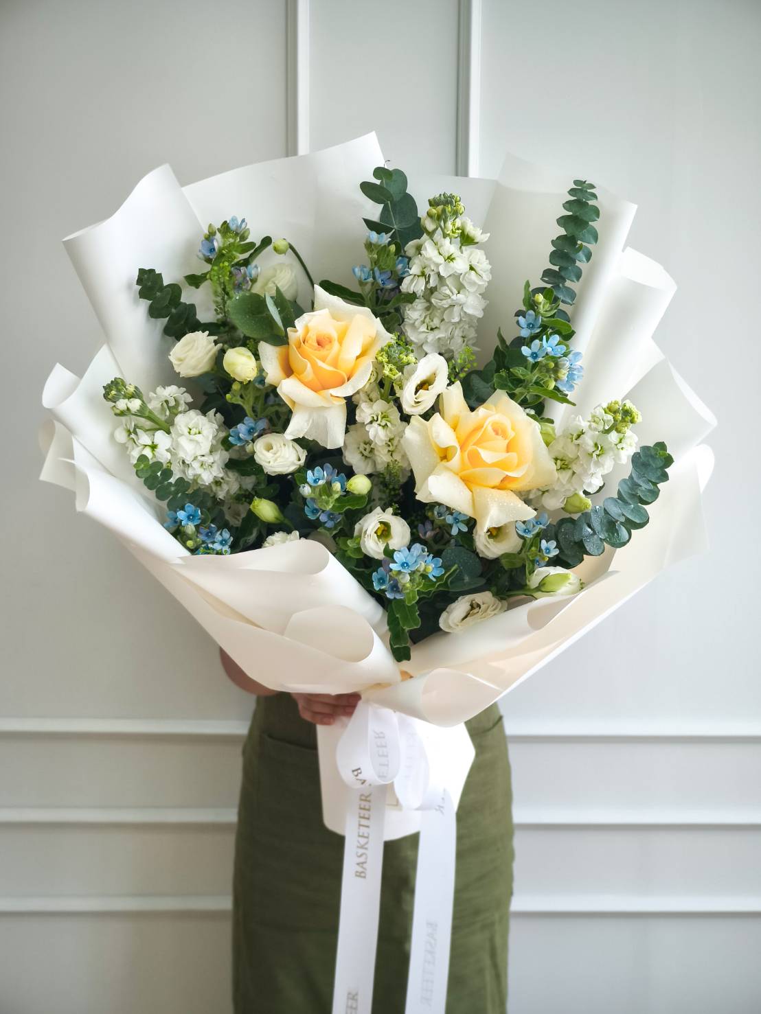 Large bouquet with yellow roses, blue flowers, white blooms, and eucalyptus wrapped in white paper – cheerful flower gift