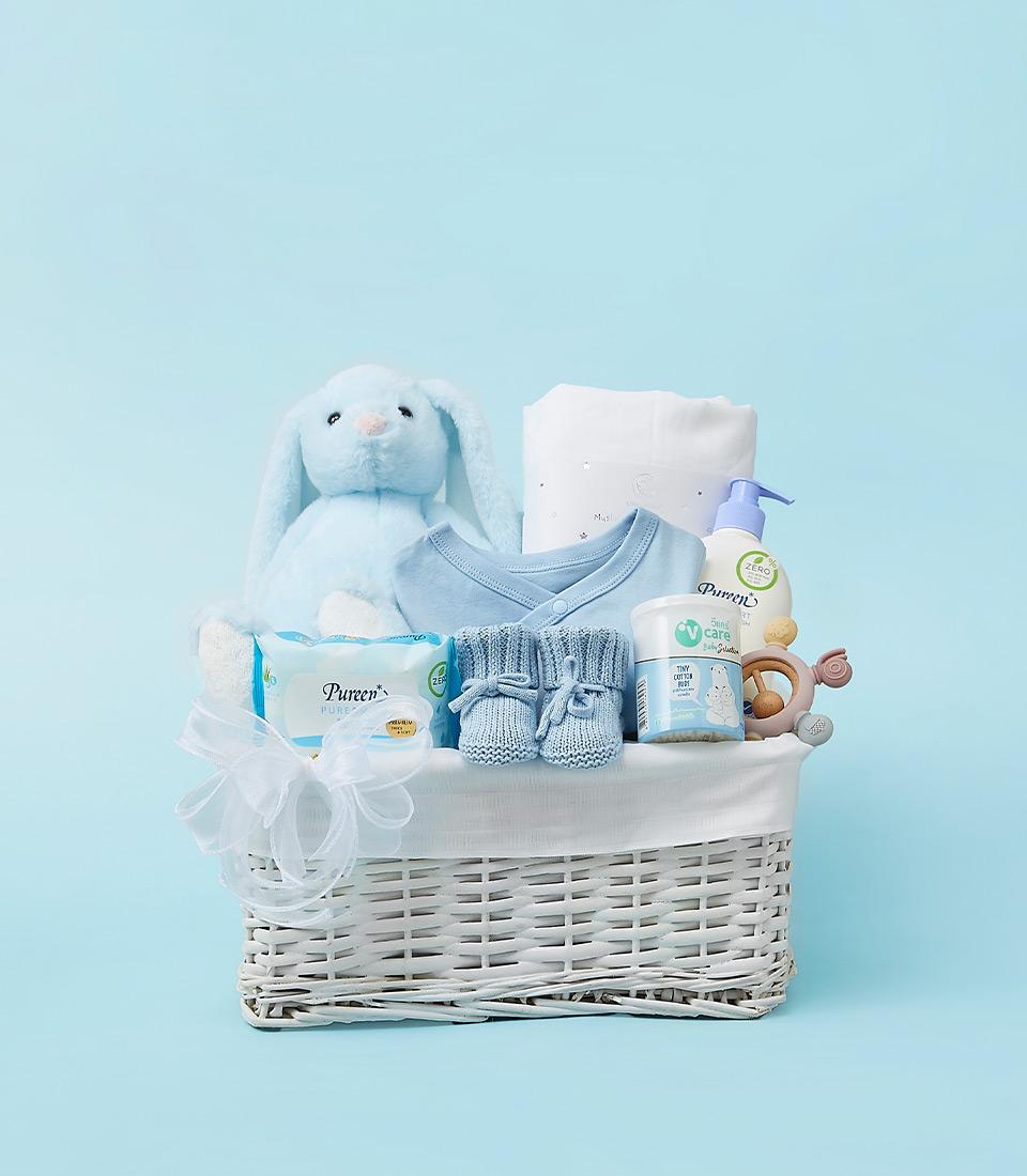 A welcoming baby gift set featuring a blue bunny, baby clothes, a towel, and gentle skincare products.
