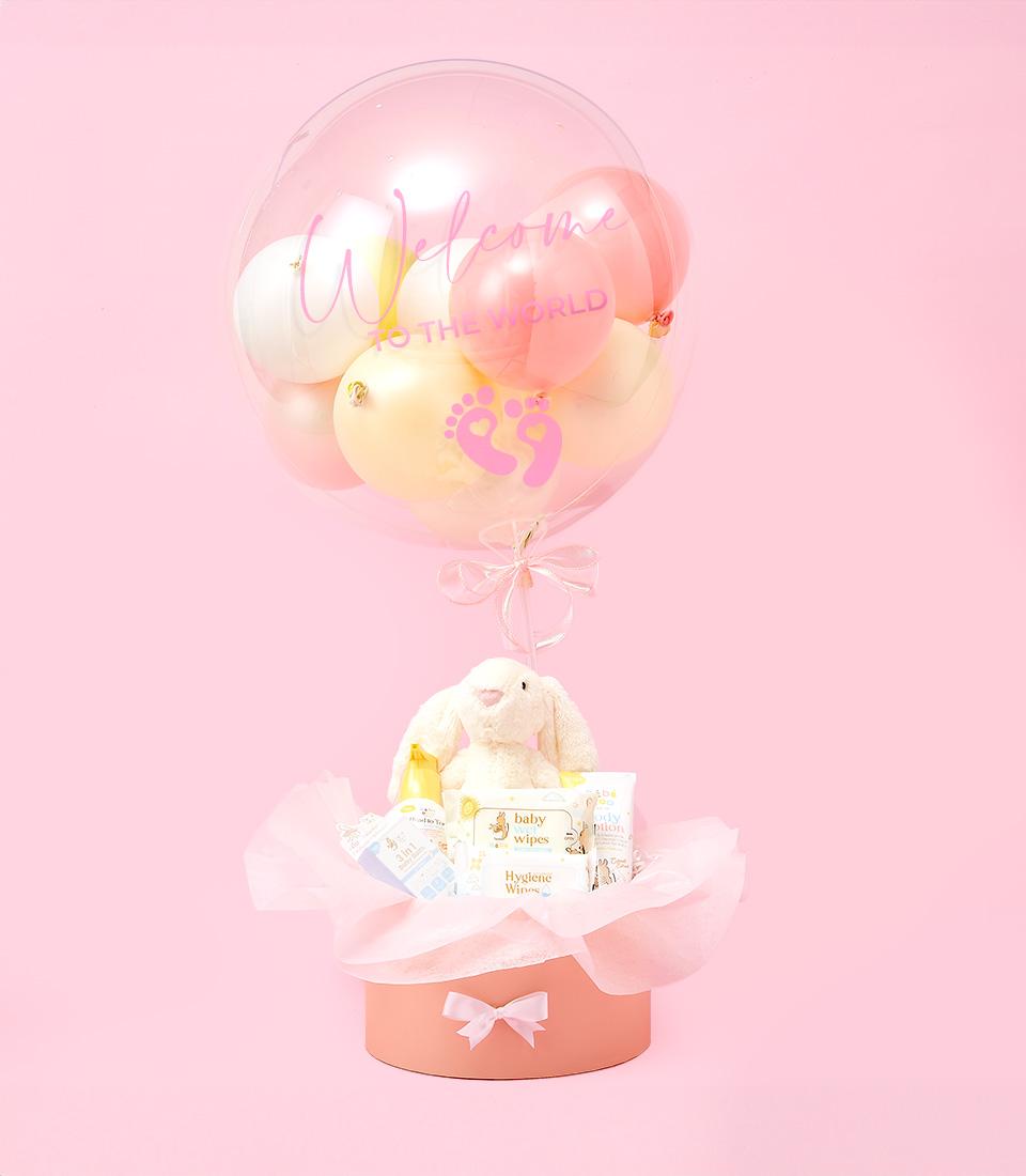 A pink gift box with a clear balloon filled with baby balloons and a plush bunny toy.