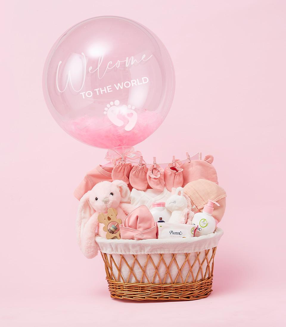 A Precious Newborn Girl Gift Basket filled with pink baby items, including a plush bunny, baby clothes, blanket, bottle, and pacifier. A large transparent balloon with 