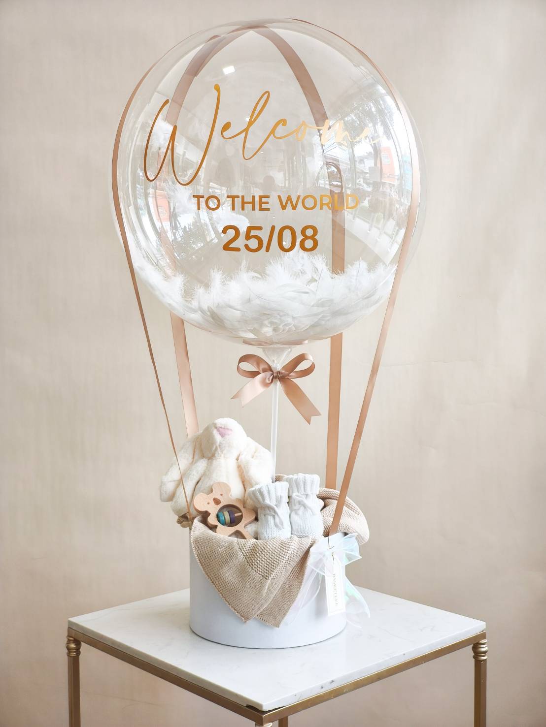 Newborn balloon gift box with personalised transparent balloon, plush toy, baby socks, and blanket in a white round box.