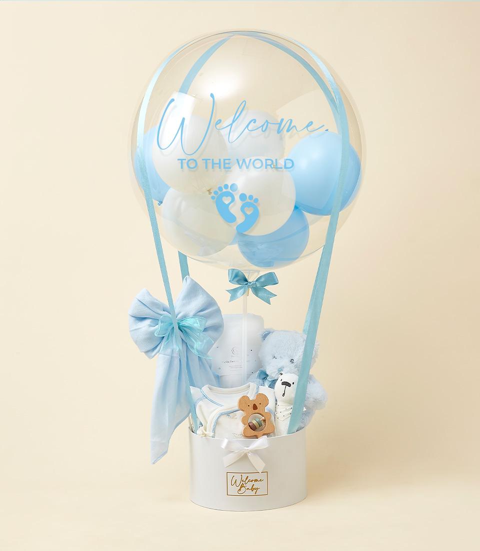 A decorative gift arrangement for a newborn baby. It features a transparent balloon filled with blue and white balloons, a 