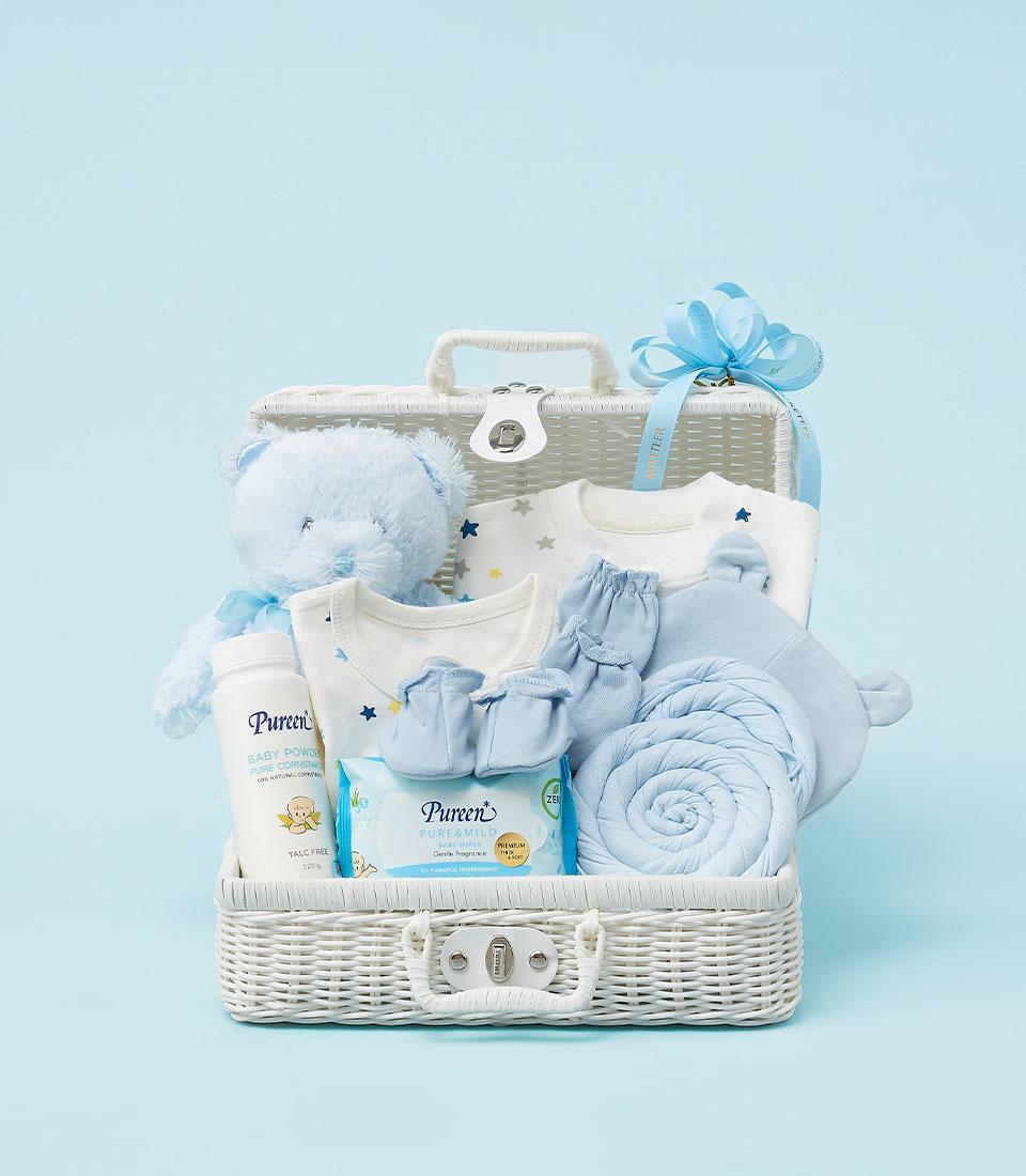 A white wicker basket filled with baby essentials, including a plush bear, clothes, a blanket, and baby powder.