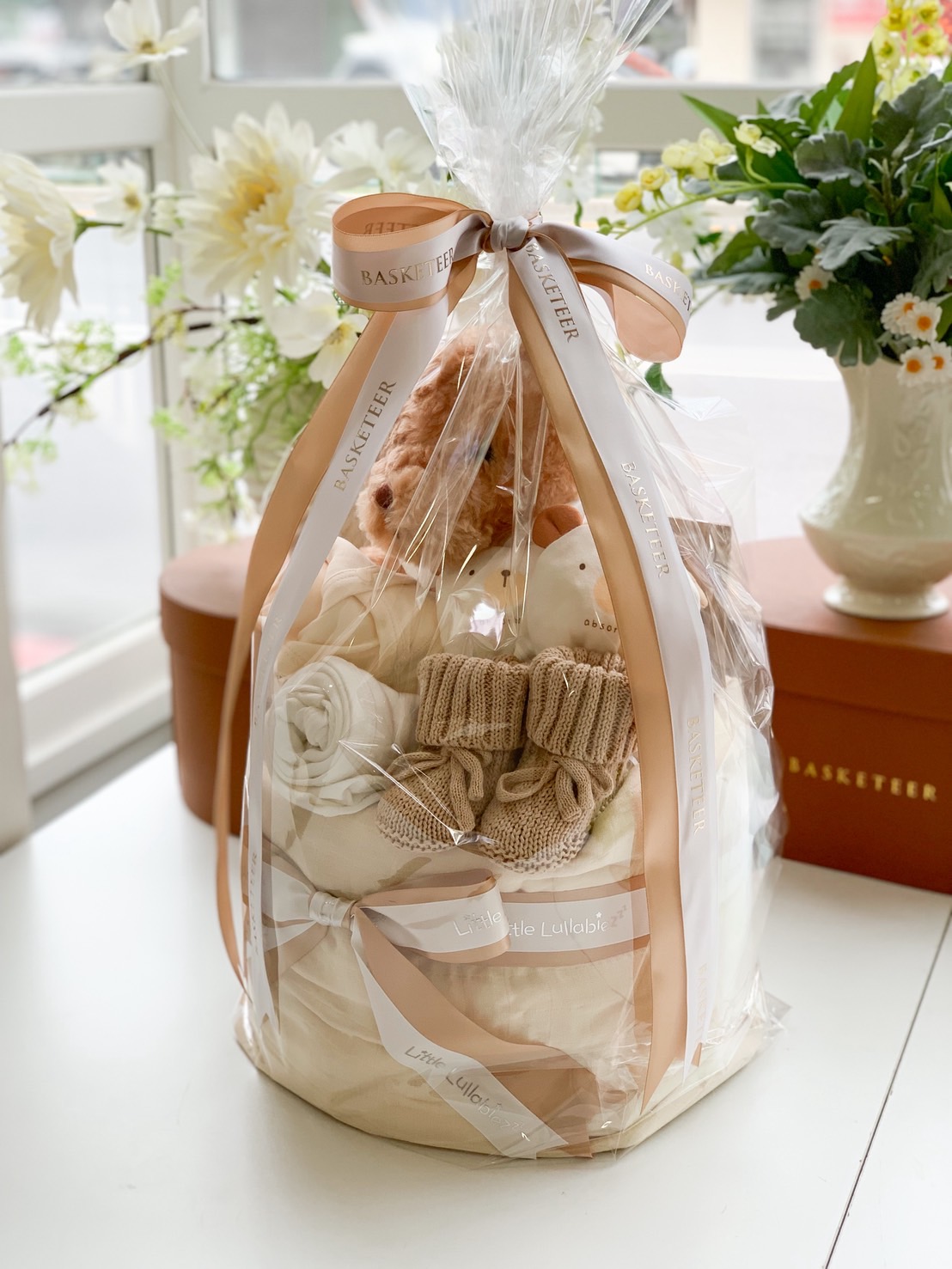 Premium neutral baby gift basket with teddy bear, baby clothes, and toys wrapped elegantly with ribbons, ideal for newborn gifts.