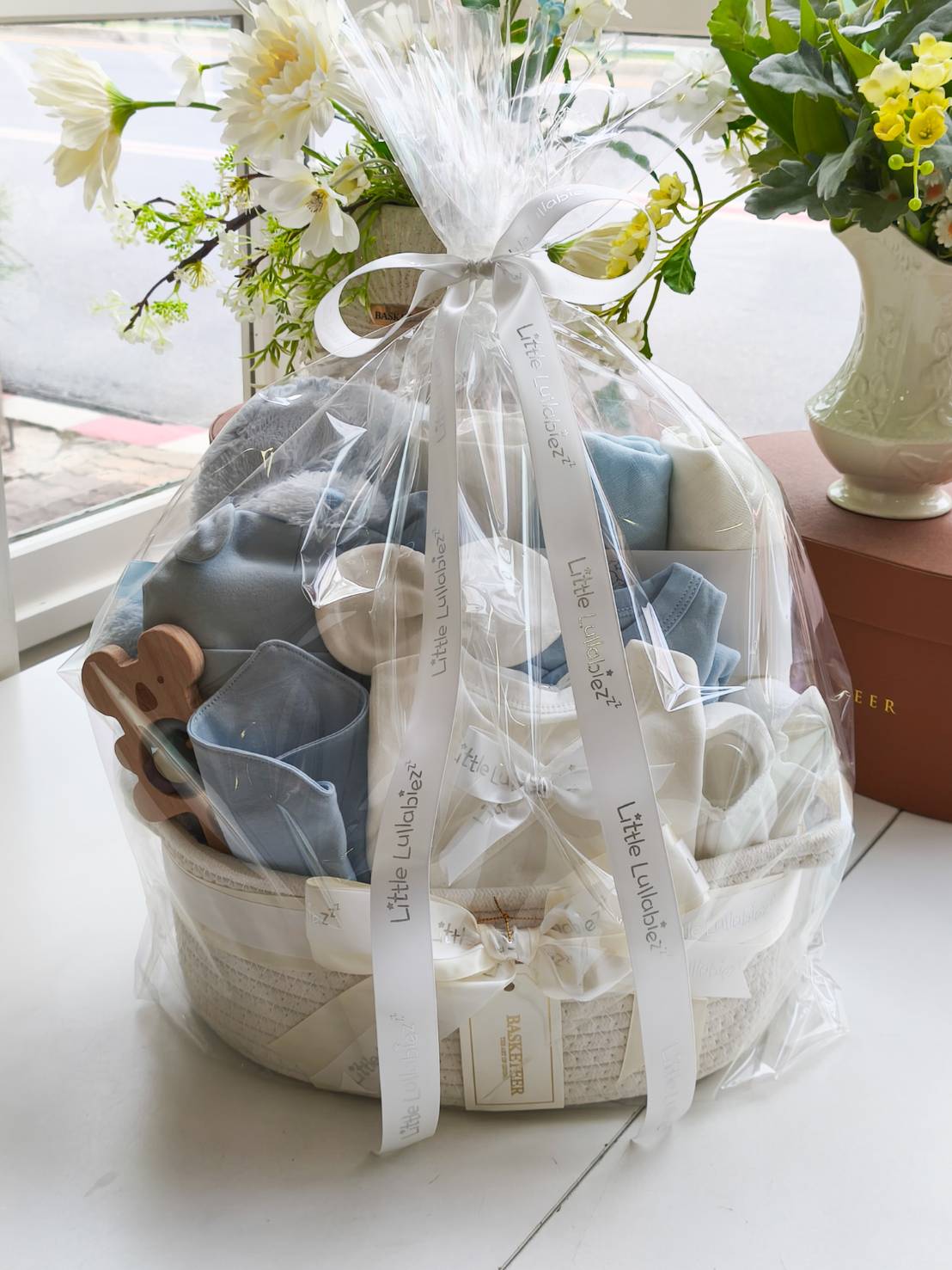 Baby boy gift basket with blue teddy bear, newborn clothes, blankets, and essentials, decorated with satin ribbon