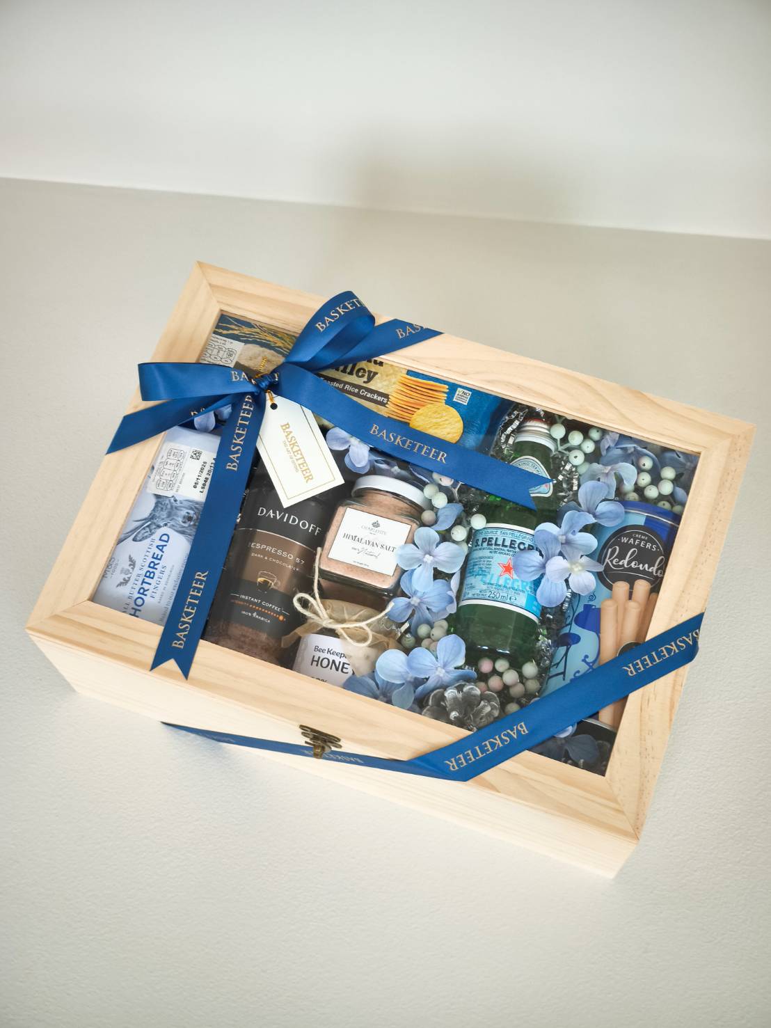 Luxury wooden gift box with blue ribbon, containing premium snacks, coffee, mineral water, honey, and gourmet treats.