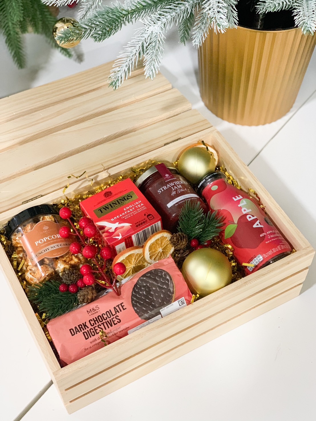 Wooden crate filled with tea, cookies, jam, juice, and festive decorations for Christmas gifting.