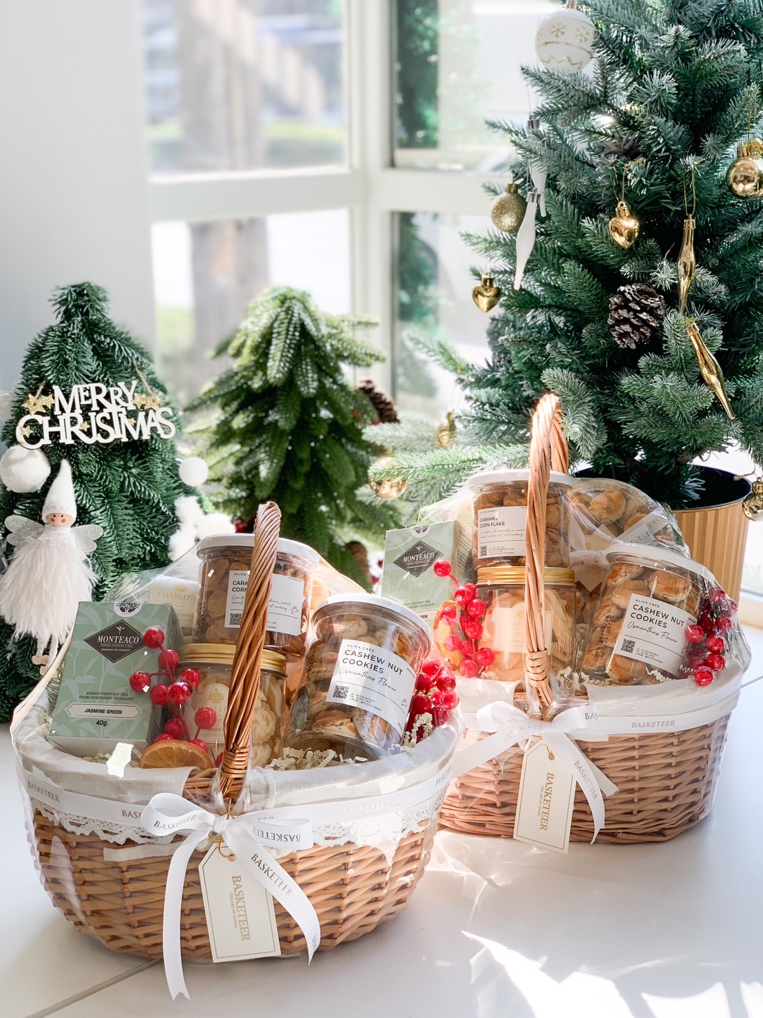 A holiday-themed gourmet basket featuring jars of cookies, Jasmine Green Tea, and festive decorations with red berries and white ribbons.