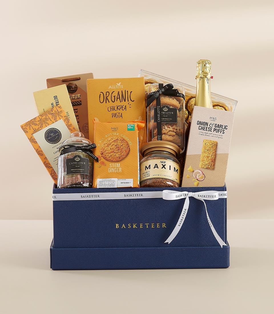 Gourmet gift hamper featuring organic chickpea pasta, ginger cookies, cheese puffs, artisan crackers, and sparkling wine.