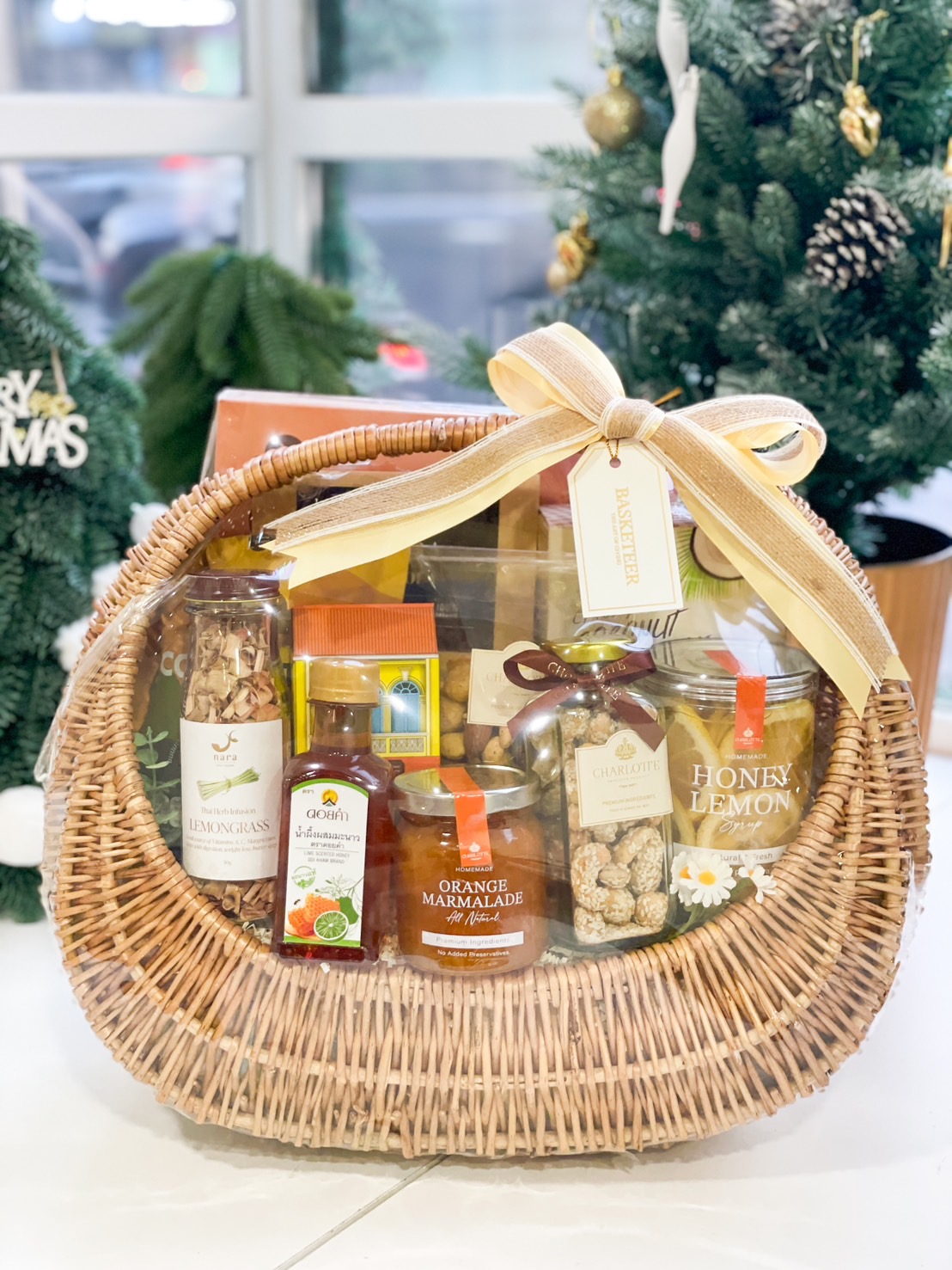 Golden wicker gift basket filled with honey lemon jars, orange marmalade, lemongrass tea, and gourmet nuts, tied with a gold ribbon.
