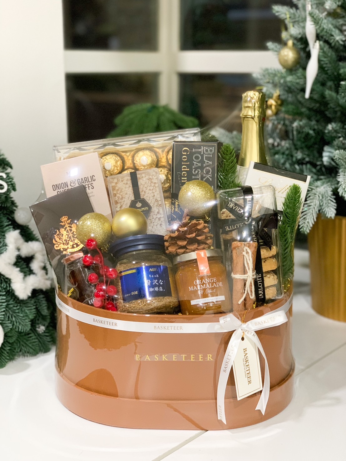 Golden gift hamper featuring sparkling wine, Ferrero Rocher chocolates, orange marmalade, premium coffee, and gourmet treats.