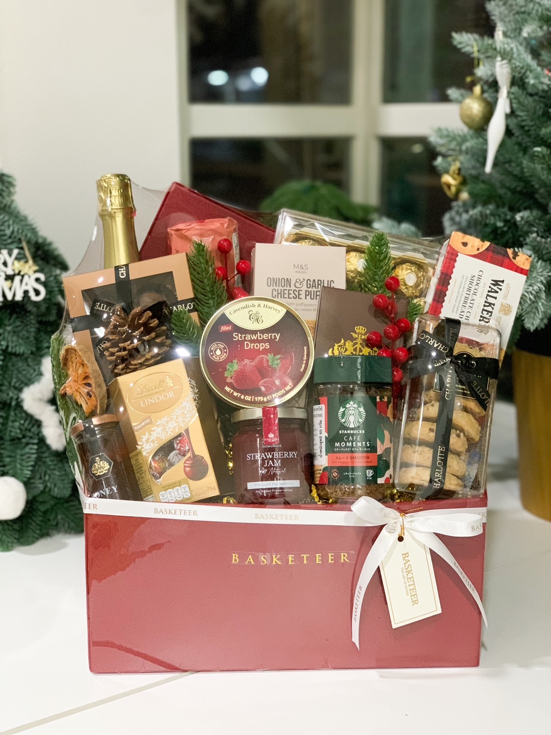 Luxurious red gift hamper with wine, Lindor chocolates, shortbread, Starbucks coffee, and festive treats.