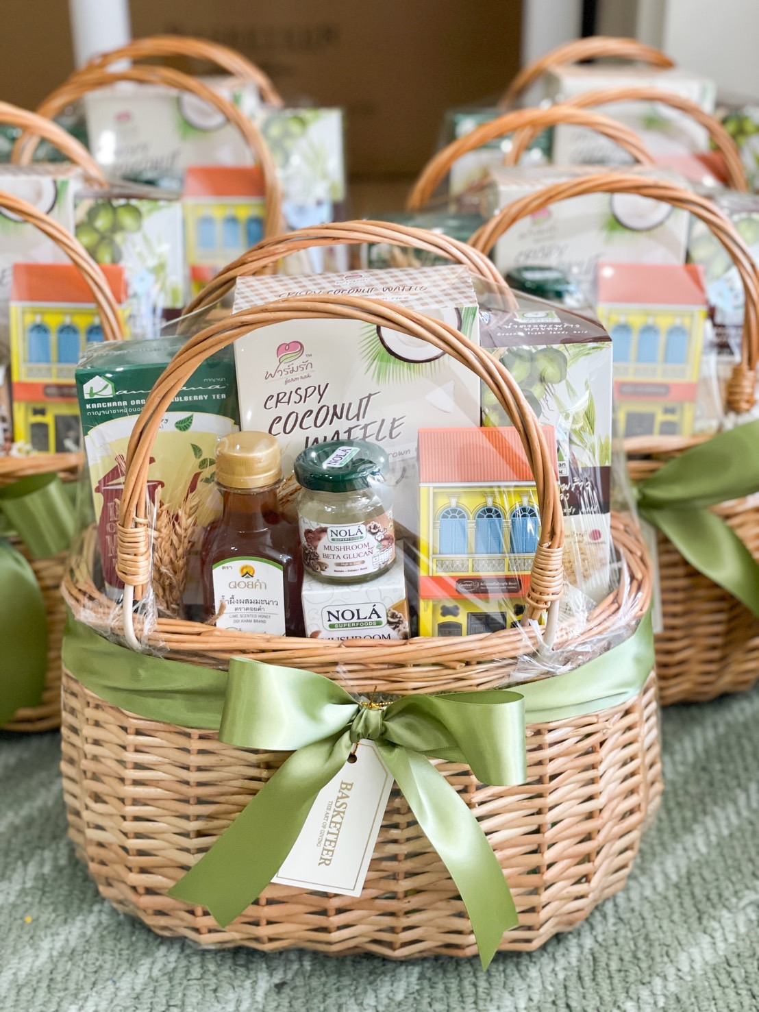 A wicker basket with a green ribbon, filled with coconut waffle snacks, mulberry tea, and NOLA mushroom beta-glucan drinks.