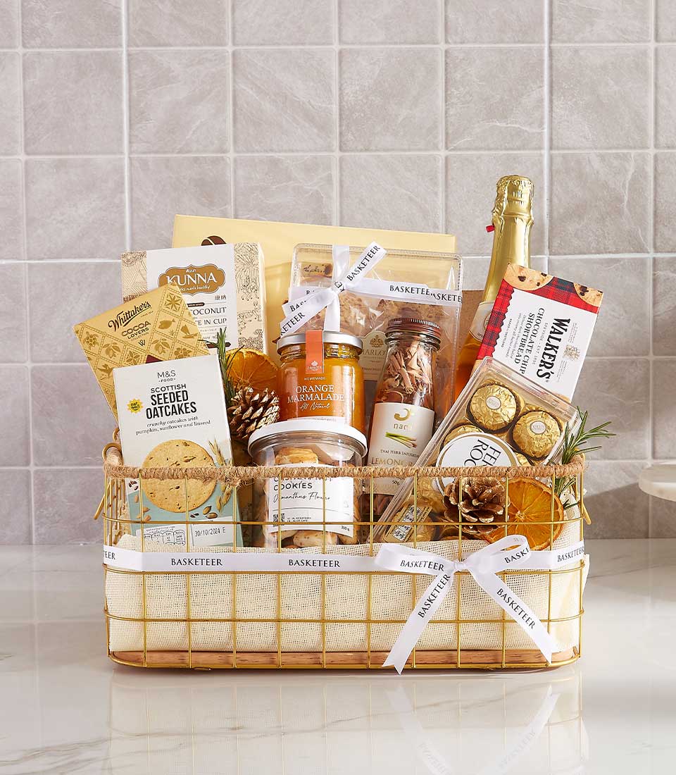 A neatly arranged luxury indulgence gift basket containing various gourmet food items, including oatcakes, chocolate, marmalade, and champagne. The basket is adorned with pinecones and ribbons labeled 