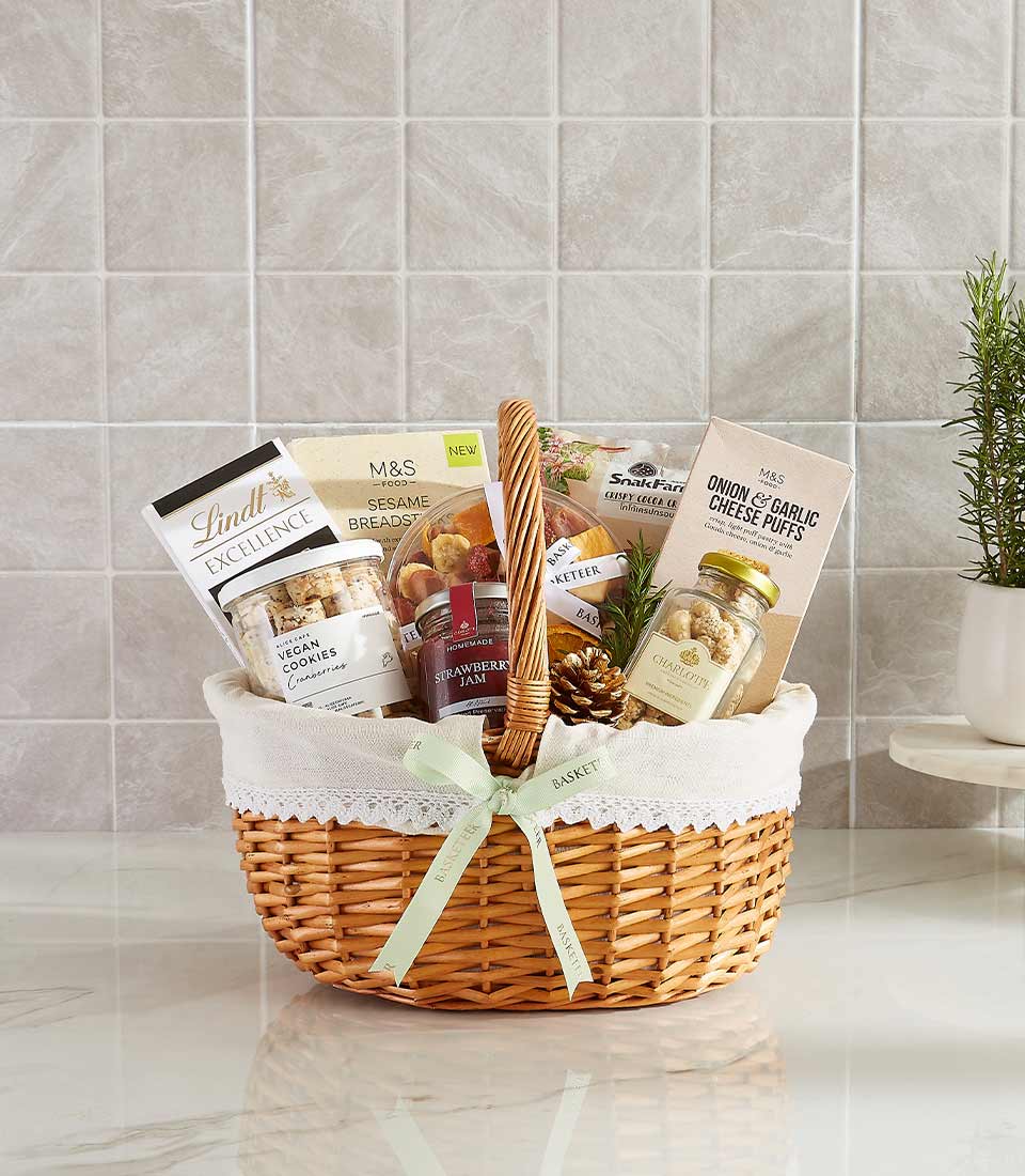 Gift basket with vegan cookies, Lindt chocolate, onion garlic cheese puffs, sesame breadsticks, and strawberry jam.