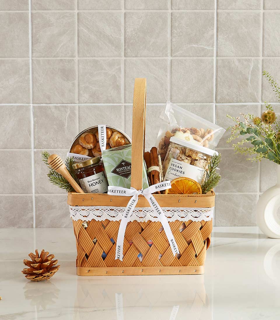 Elegant woven gift basket with honey, herbal tea, vegan cookies, and mixed nuts.