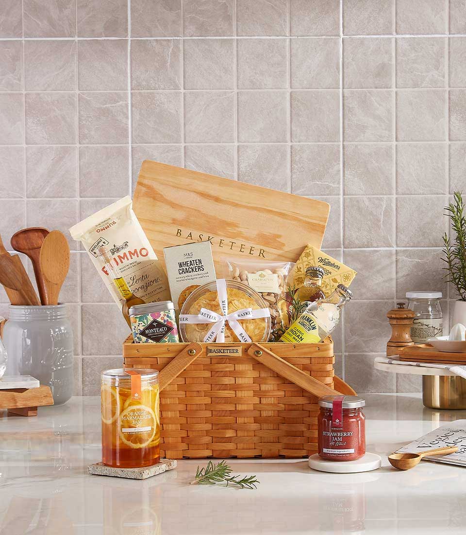 Gourmet picnic basket with crackers, pasta, jams, and assorted snacks in a woven basket, ideal for gifting and outdoor gatherings.