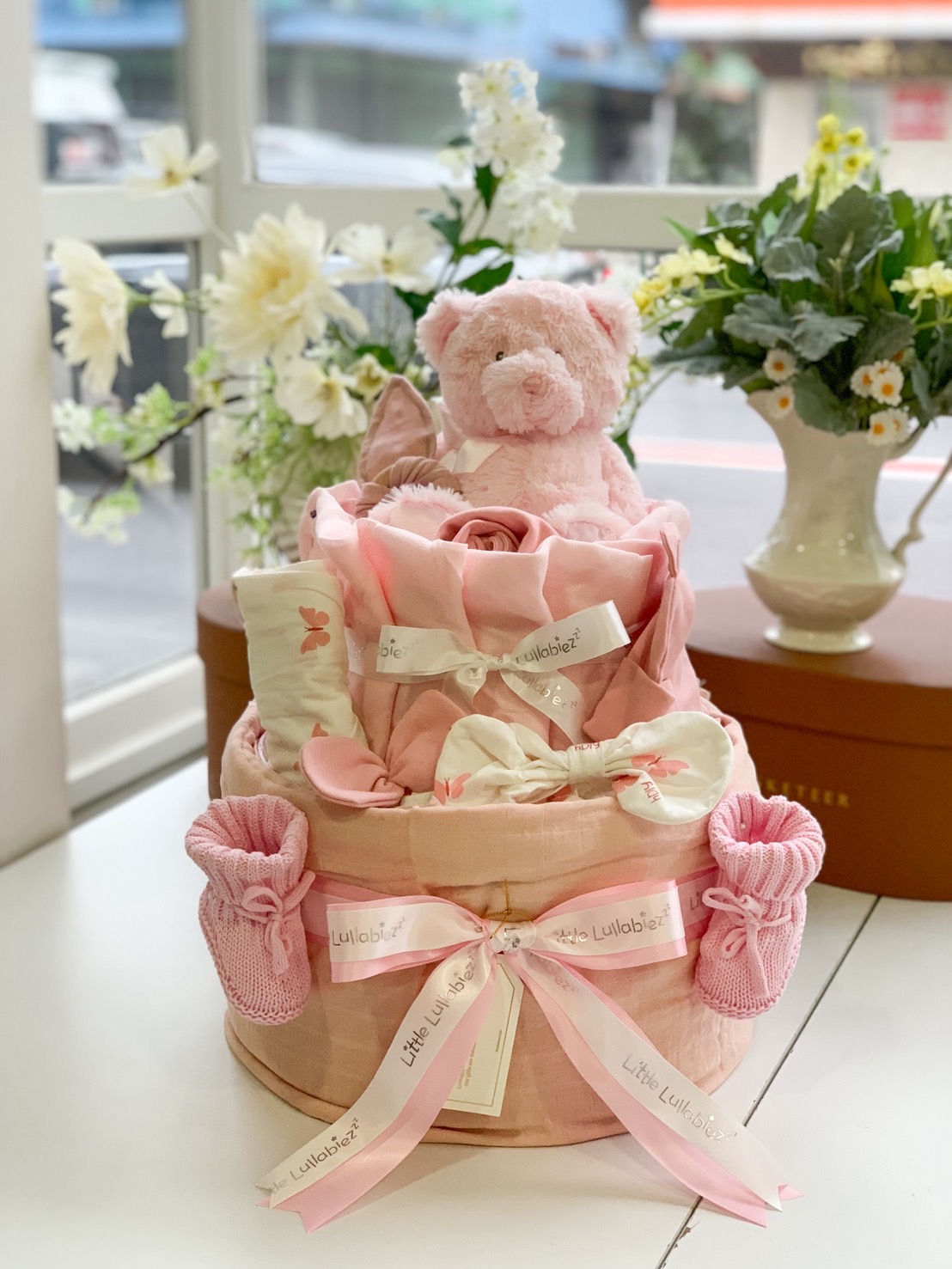 Pink baby girl gift hamper with teddy bear, baby clothes, mittens, and decorative ribbons by Little Lullabiez.