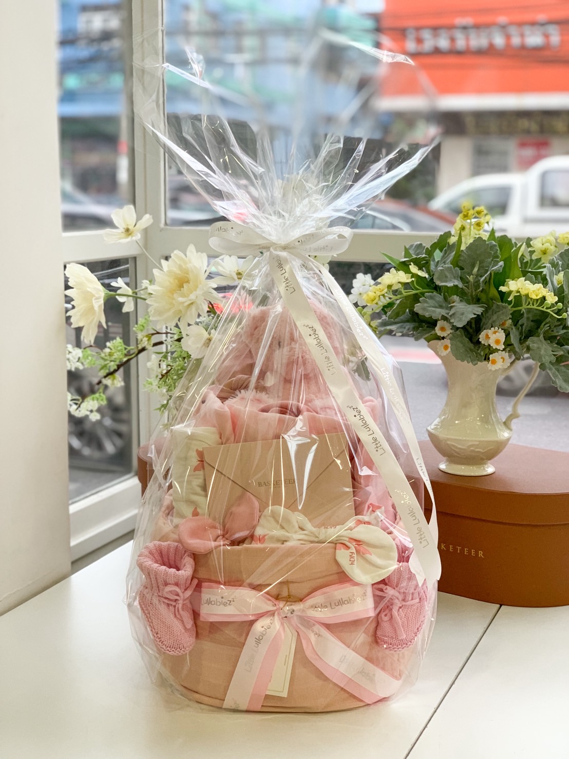 Wrapped pink baby girl gift set with teddy bear, newborn clothes, mittens, and ribbon packaging by Little Lullabiez.