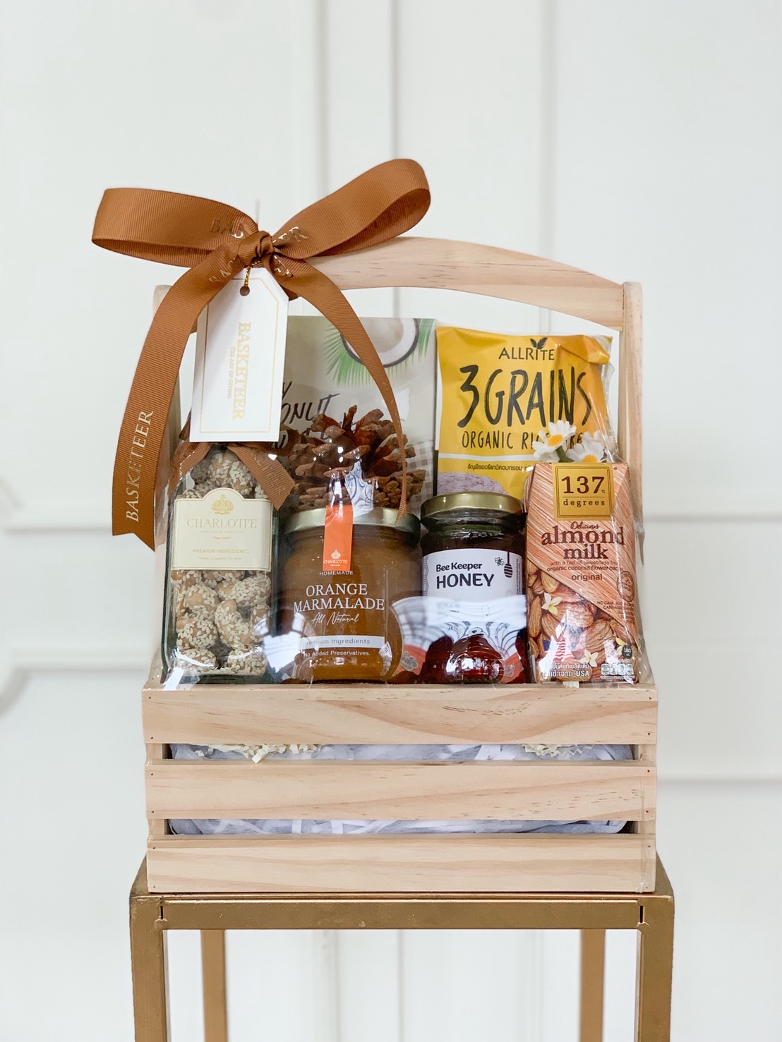 Healthy gift crate featuring almond milk, orange marmalade, honey, granola, and organic grains, in a wooden box with a brown ribbon.