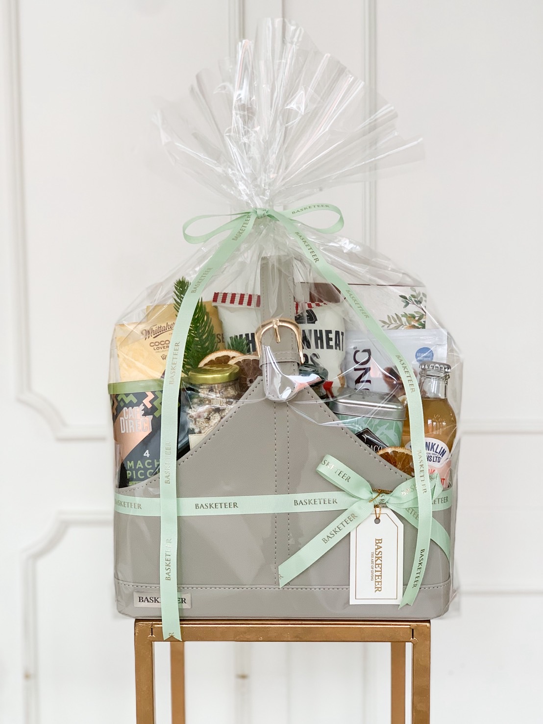 Premium sage green leather hamper filled with sparkling drinks, healthy snacks, and festive packaging with pastel green ribbon.