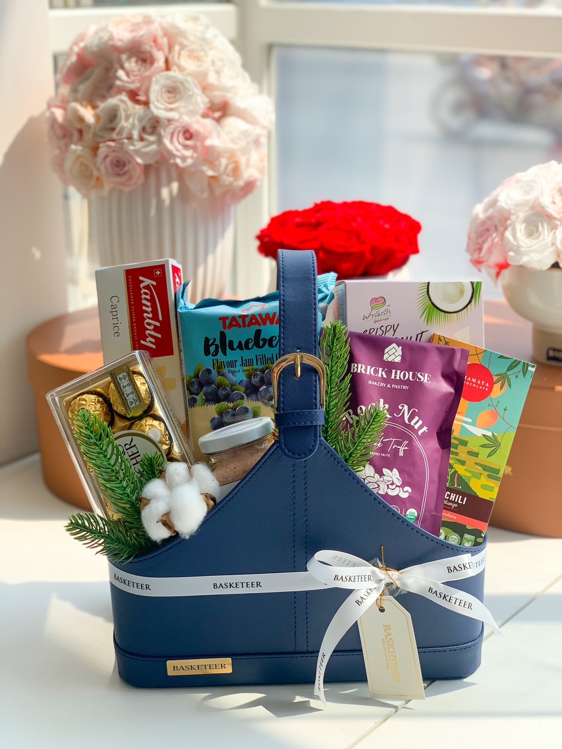 A luxurious navy blue leather tote filled with premium gourmet treats, beautifully arranged with Basketeer branding and elegant decorative accents.