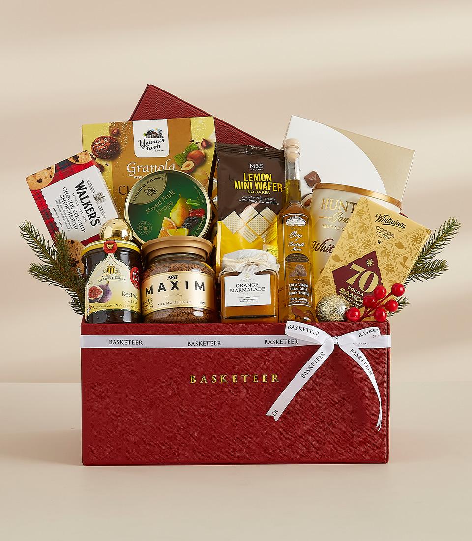 A red gift box filled with a variety of gourmet food items, including chocolates, biscuits, snacks, and drinks.