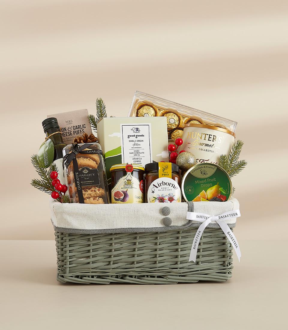 A grey wicker basket filled with a variety of gourmet food items, including chocolates, biscuits, snacks, and drinks.
