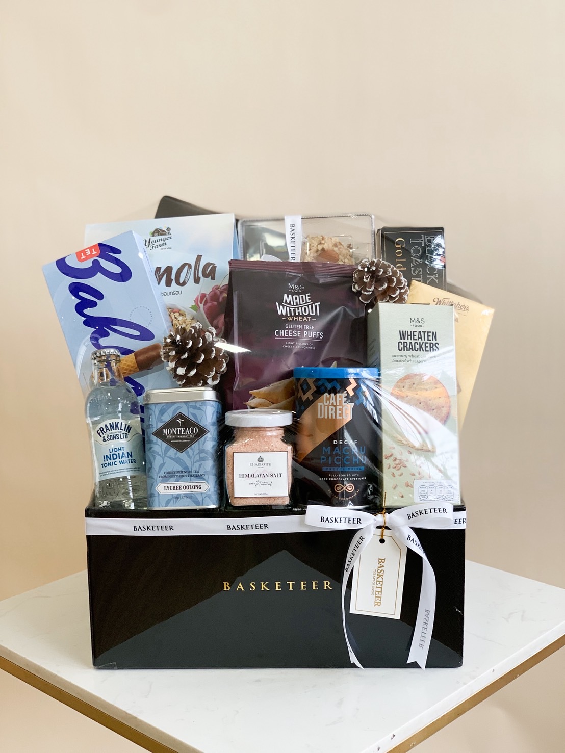 Luxury black gift box filled with healthy treats: granola, oolong tea, pink Himalayan salt, gluten-free cheese puffs, crackers, and tonic water.