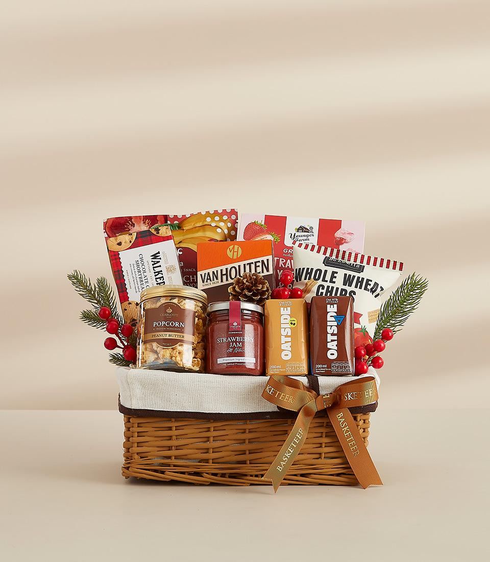 A wicker basket filled with a variety of snacks, including chocolates, biscuits, popcorn, and jam.