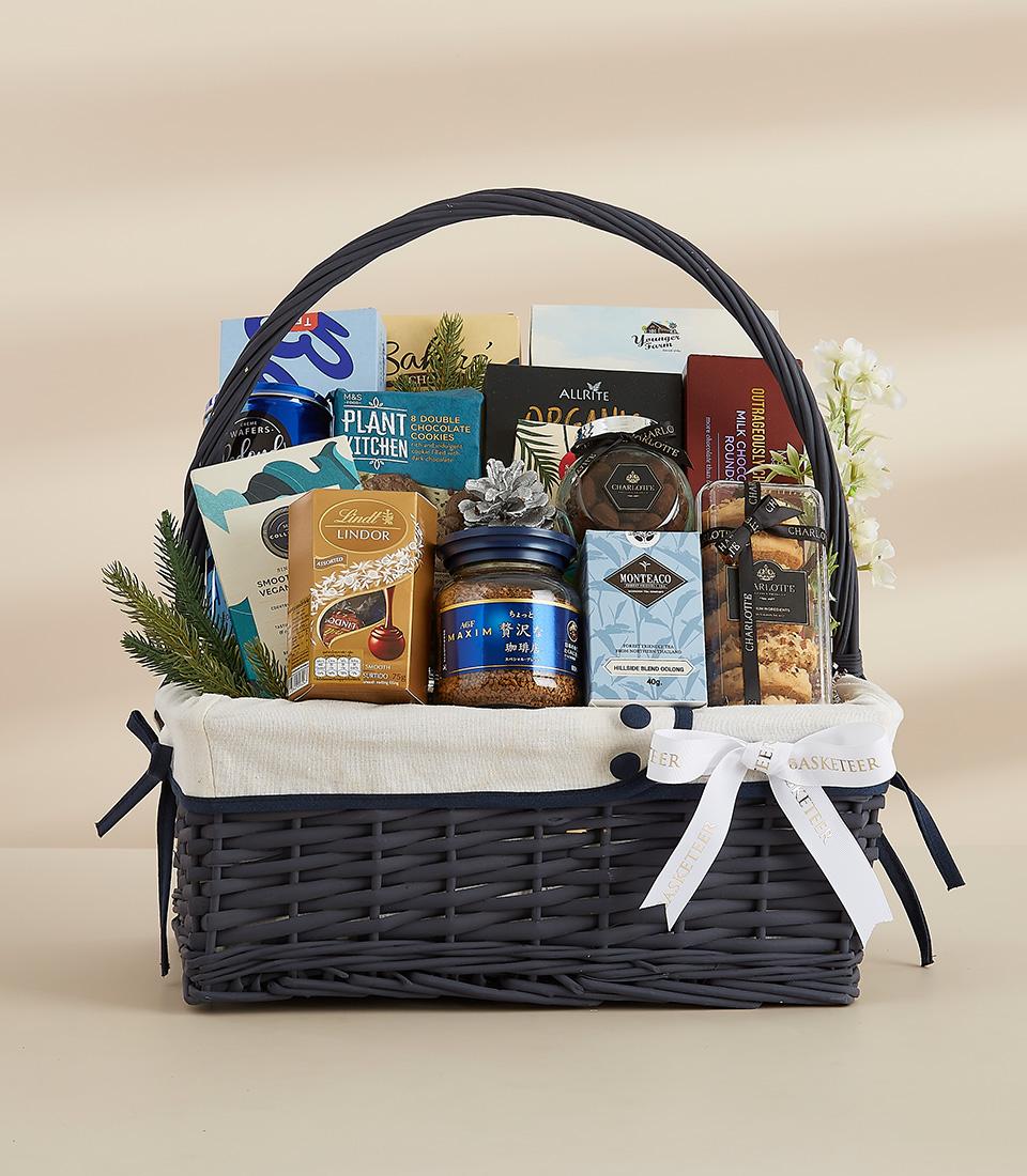 A blue wicker basket filled with a variety of gourmet food items, including coffee, chocolate, and snacks.