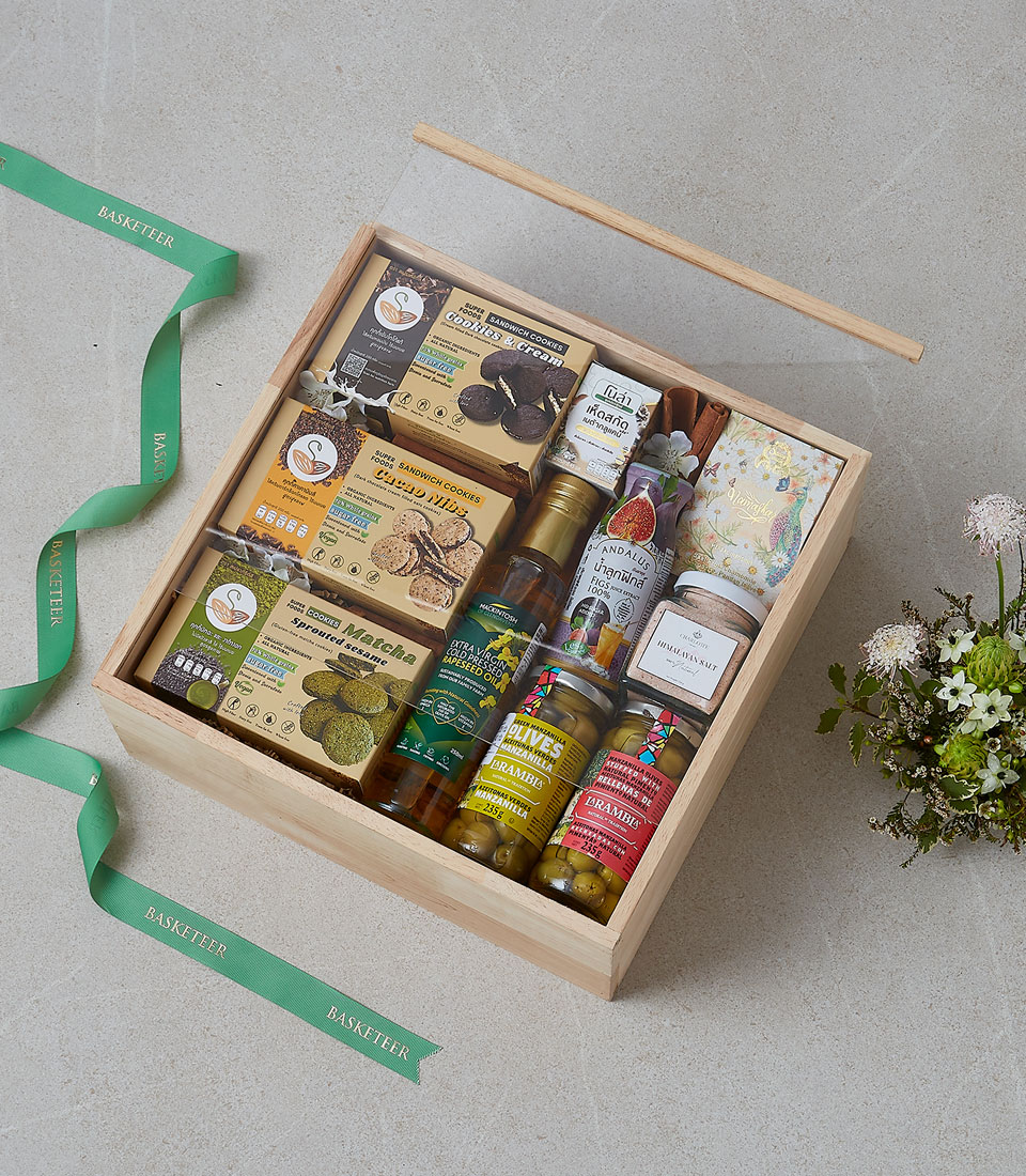 Premium wooden gift box featuring healthy treats including matcha cookies, honey, herbal tea, olives, seed crackers, and gourmet condiments.