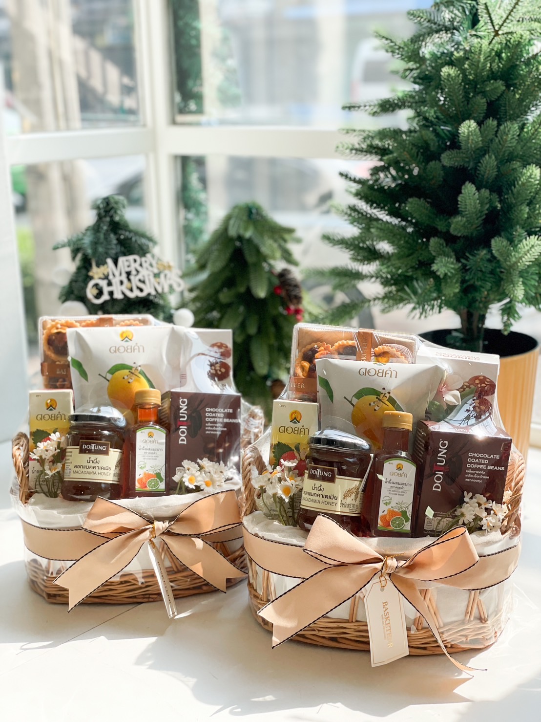 Health-themed gift basket with Doi Tung macadamia honey, herbal tea, coffee beans, and premium snacks, wrapped in a wicker basket with a beige bow.