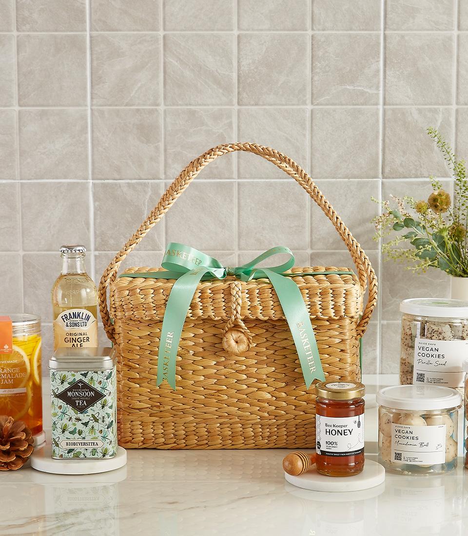 Woven basket with honey, ginger ale, herbal tea, and vegan cookies.
