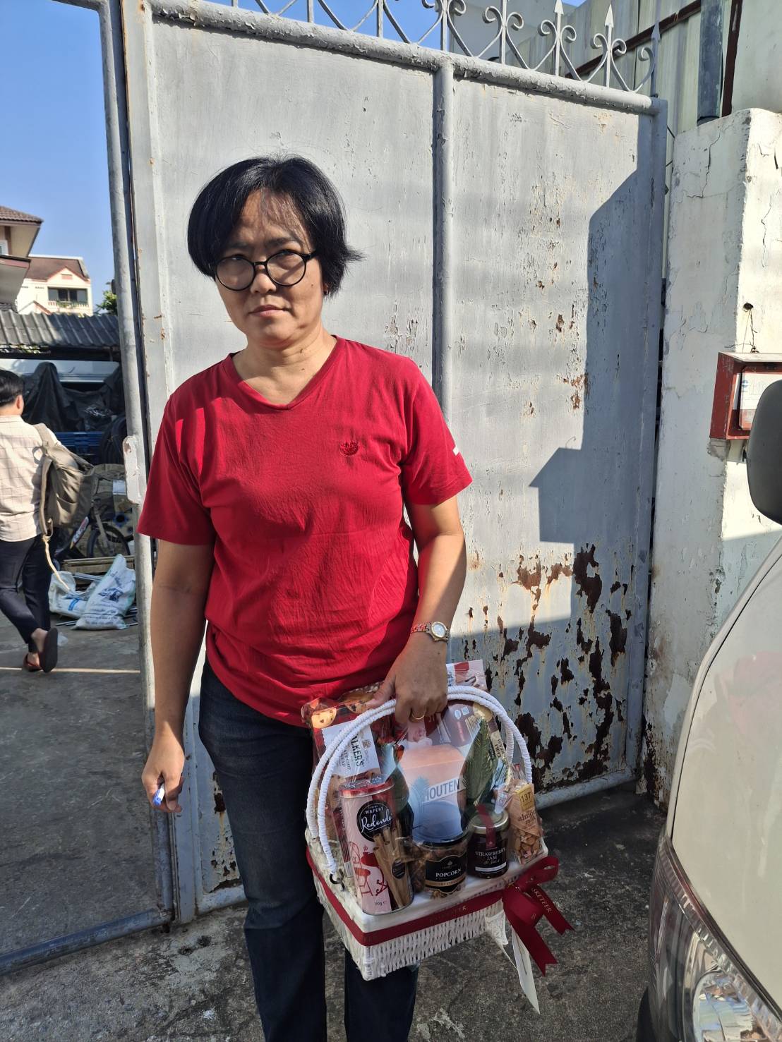Customer holding a premium gift basket filled with beautifully arranged items, standing in front of a gate with a satisfied expression
