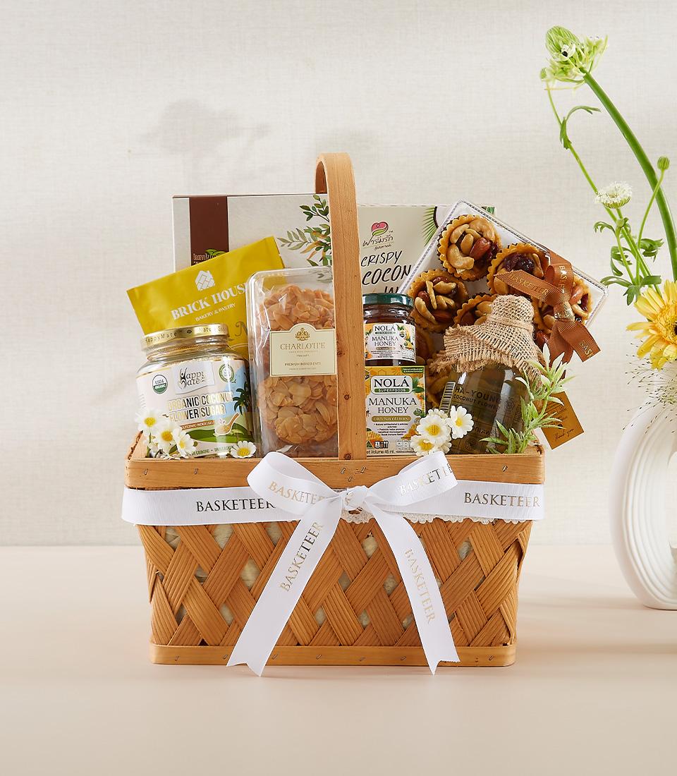 Gift basket with Manuka honey, crispy coconut, flower seed crackers, and assorted gourmet snacks.
