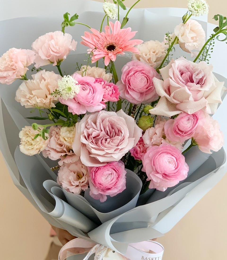 Close-up of a pink mixed bouquet with roses, carnations, and ranunculus in soft wrapping.