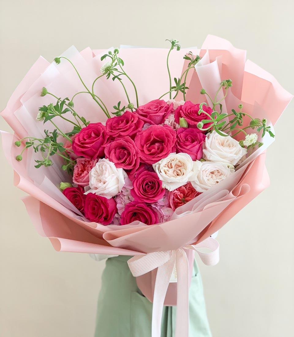 Bouquet of pink and white roses wrapped in soft pink paper.