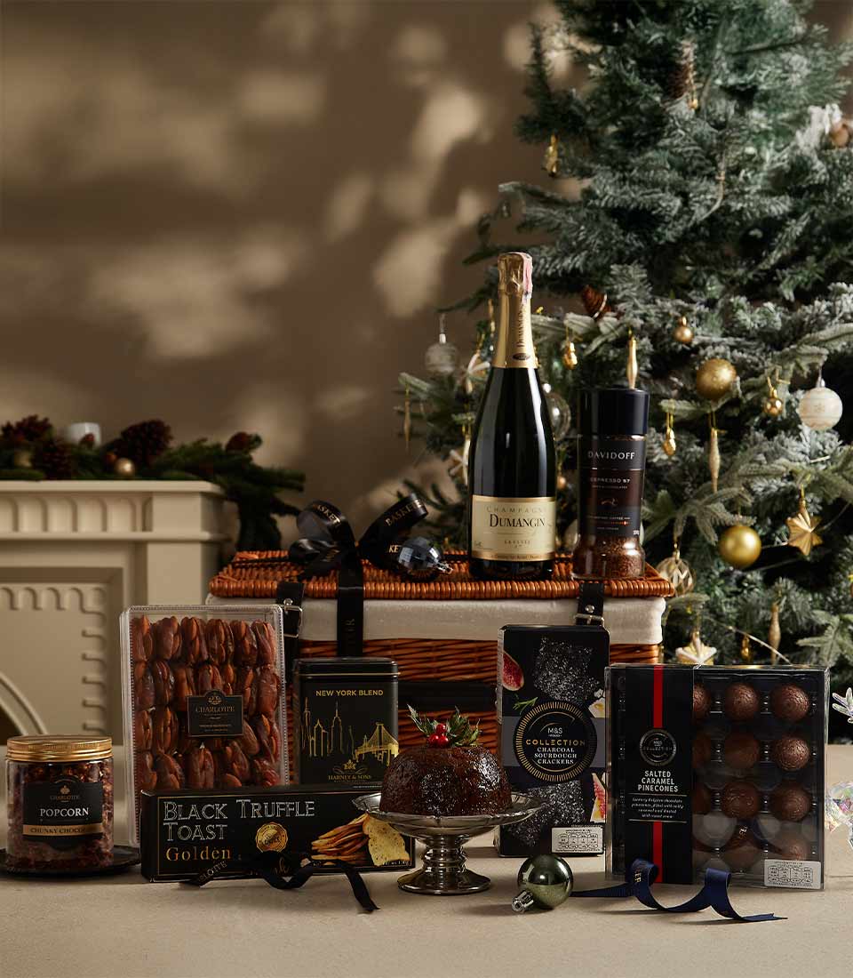 An elegant wicker basket with Dumangin Champagne, Davidoff coffee, black truffle toast, salted caramel truffles, Christmas pudding, chewy popcorn, and tea, displayed in a festive setting with a Christmas tree in the background.