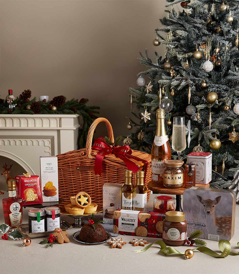 Luxury Christmas hamper with gourmet snacks, chocolates, shortbread, and festive delicacies, set near a Christmas tree.