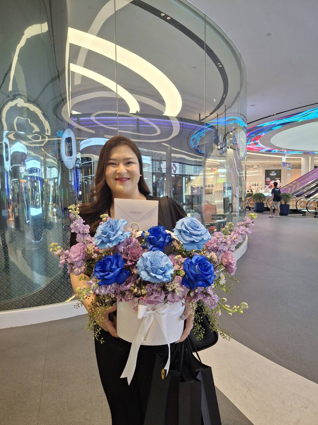 A woman holding a white hatbox filled with vibrant royal blue roses and soft purple flowers, perfect for elegant gifting.