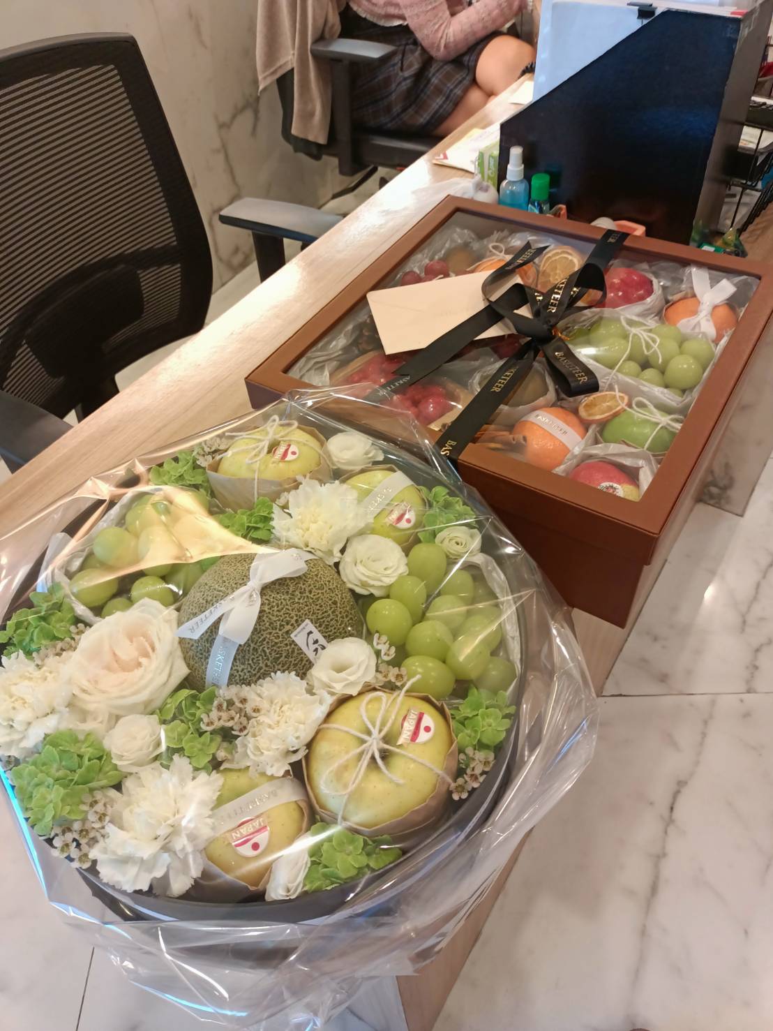 A premium fruit and floral gift set with Japanese musk melon, grapes, pears, and fresh flowers, elegantly arranged in a circular tray and wooden box.