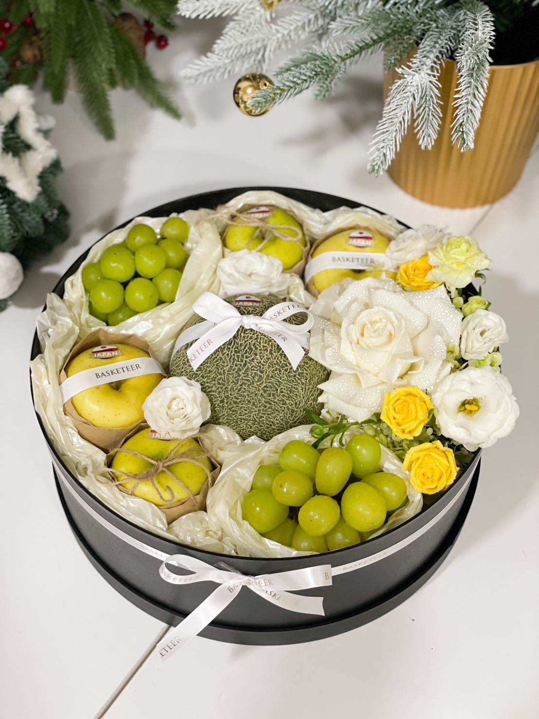Round gift box with premium Japanese fruits, green grapes, and floral decorations by Basketeer.